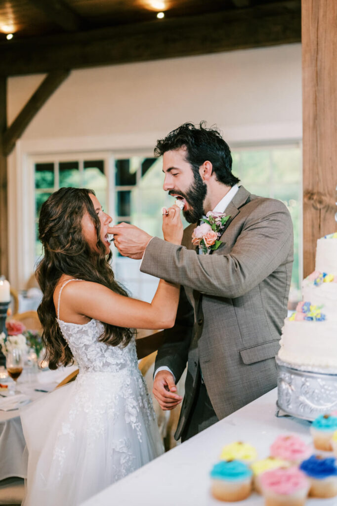 Bride and groom share wedding cake at Asheville mountain venue – The newlyweds playfully feed each other wedding cake, capturing a sweet and joyful moment at their elegant Asheville wedding reception.