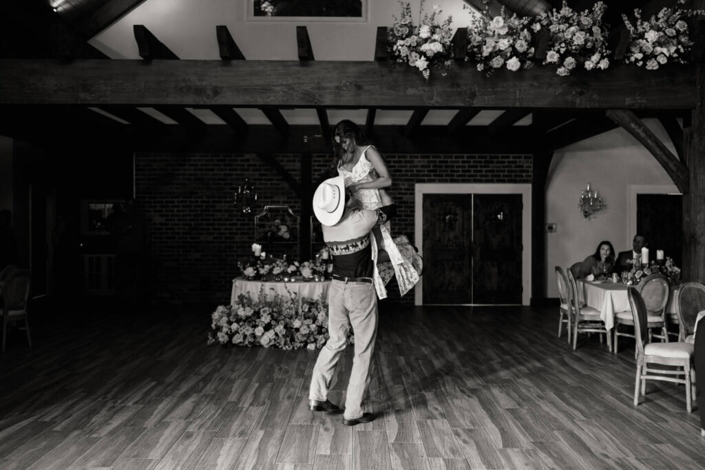 Black and white image of groom lifting bride on dance floor – The groom sweeps his bride off her feet during a romantic dance, captured in a cinematic black and white moment at their elegant Asheville wedding venue.