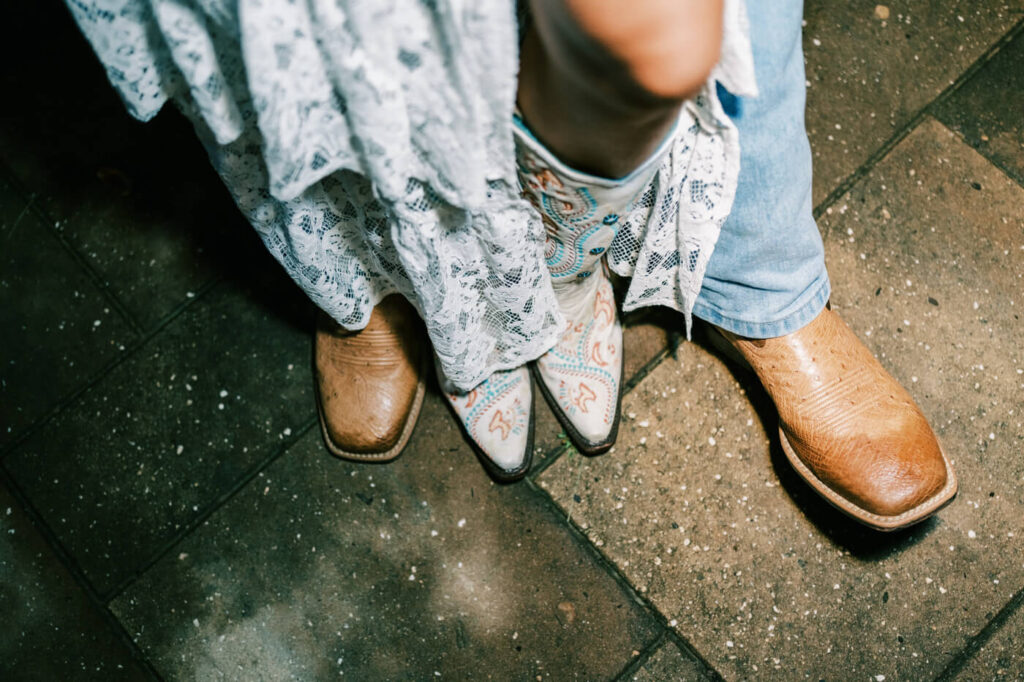 Close-up of bride and groom’s cowboy boots on wedding night – A detailed shot of the couple’s boots—lace-trimmed white boots for the bride and classic cowboy boots for the groom—perfectly embodying their rustic Asheville wedding style.