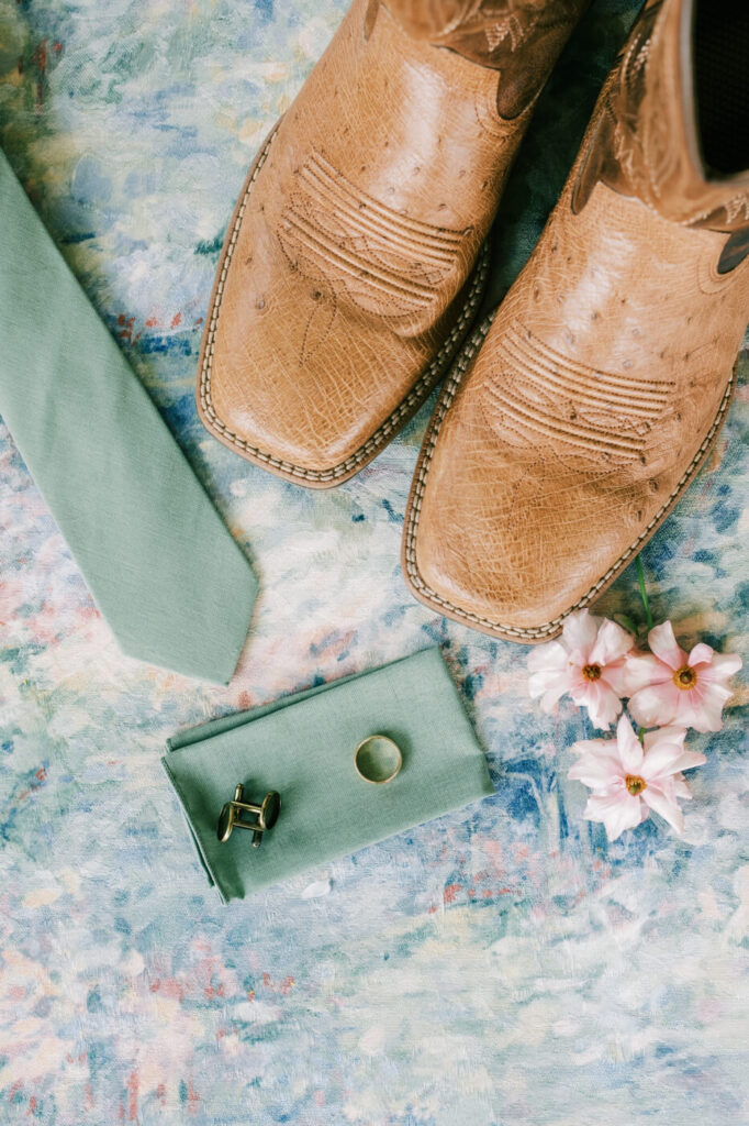 Groom’s cowboy boots, tie, and ring on a colorful fabric, detail from an Asheville mountain wedding by The Reeses.