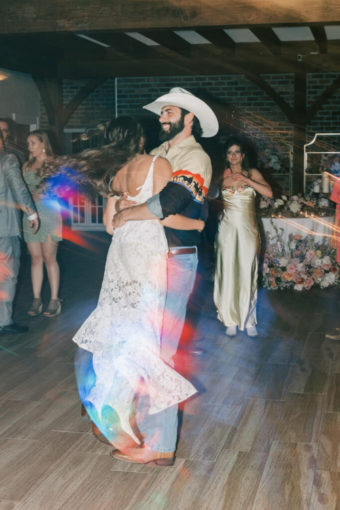 Bride and groom dancing with vibrant light trails at reception – The newlyweds spin on the dance floor, with colorful lights creating a dynamic and energetic atmosphere during their Asheville wedding celebration.