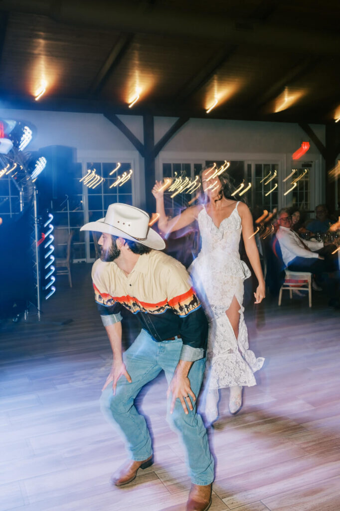 Rustic barn wedding reception dance – A bride in a lace gown twirls her groom, dressed in a western-style shirt and cowboy hat, as they celebrate their Asheville mountain wedding with a lively dance.