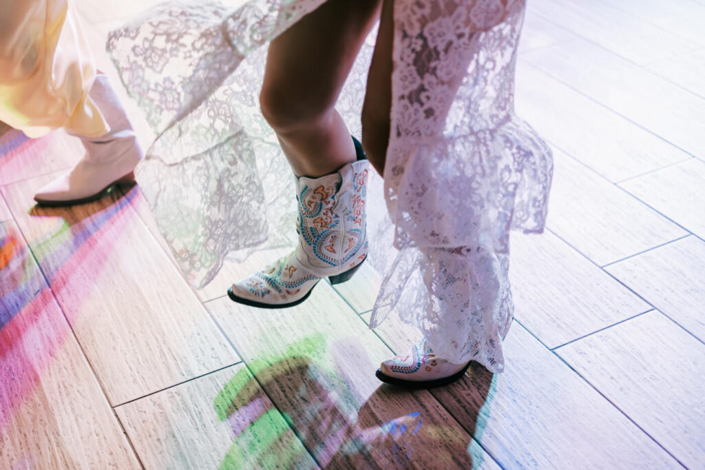 Close-up of bride’s western wedding boots – The bride’s embroidered cowboy boots peek from beneath her lace wedding dress, capturing the rustic elegance of her Asheville wedding celebration.