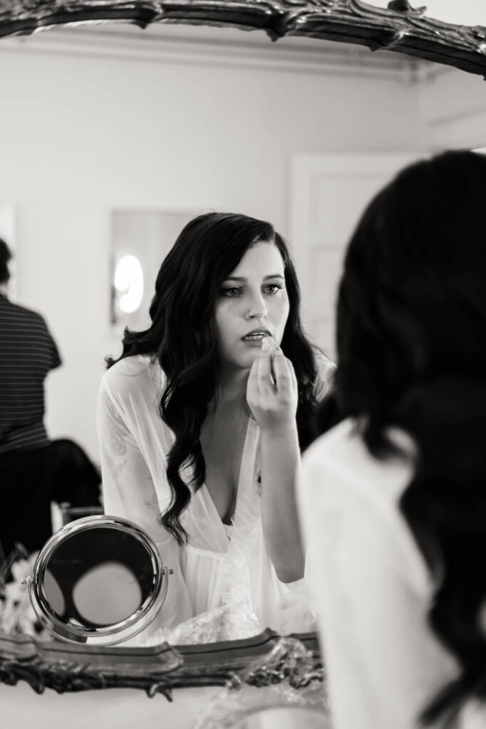 Bride Getting Ready in Mirror Reflection – A black and white portrait of the bride applying lipstick in the vintage bridal suite mirror, radiating timeless elegance.