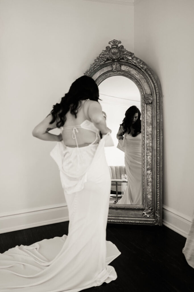 Bride Getting Ready at McAlister-Leftwich House – A romantic black-and-white image of the bride adjusting her wedding gown in front of an ornate mirror, capturing a quiet moment of reflection before the ceremony.