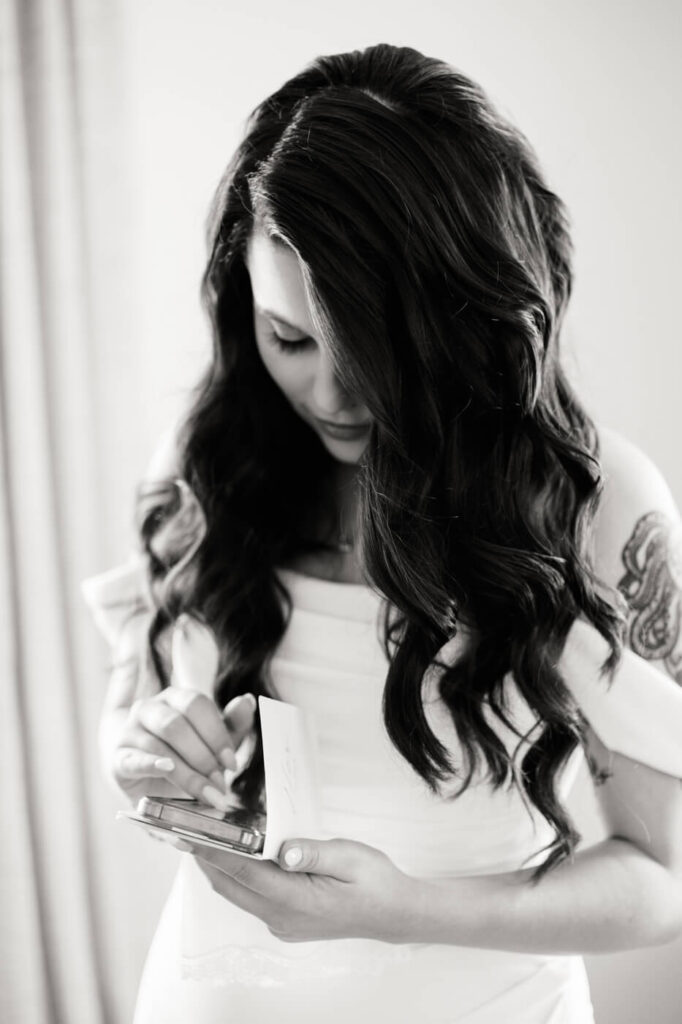 Bride reading a handwritten letter on her wedding day – A black-and-white photo of a bride with long, wavy hair in an off-the-shoulder wedding gown, reading an intimate letter before her ceremony at McAlister-Leftwich House in Greensboro, NC.