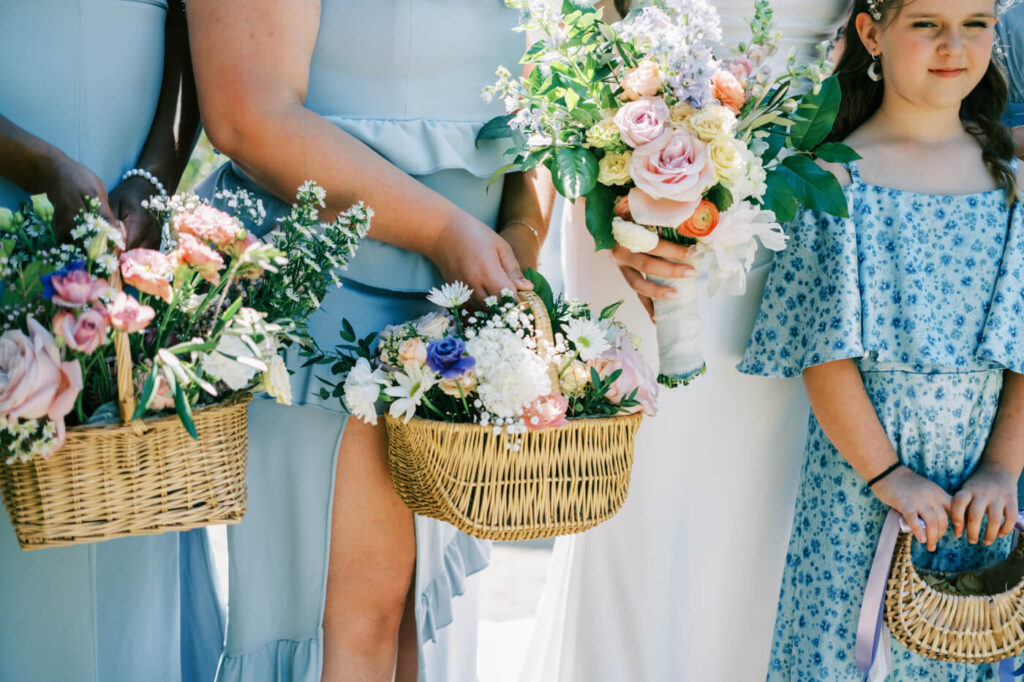 Close-up of wedding flowers in natural wicker baskets – A detailed shot of pastel wedding florals arranged in elegant wicker baskets, complementing the soft blue tones of the bridesmaids’ dresses.