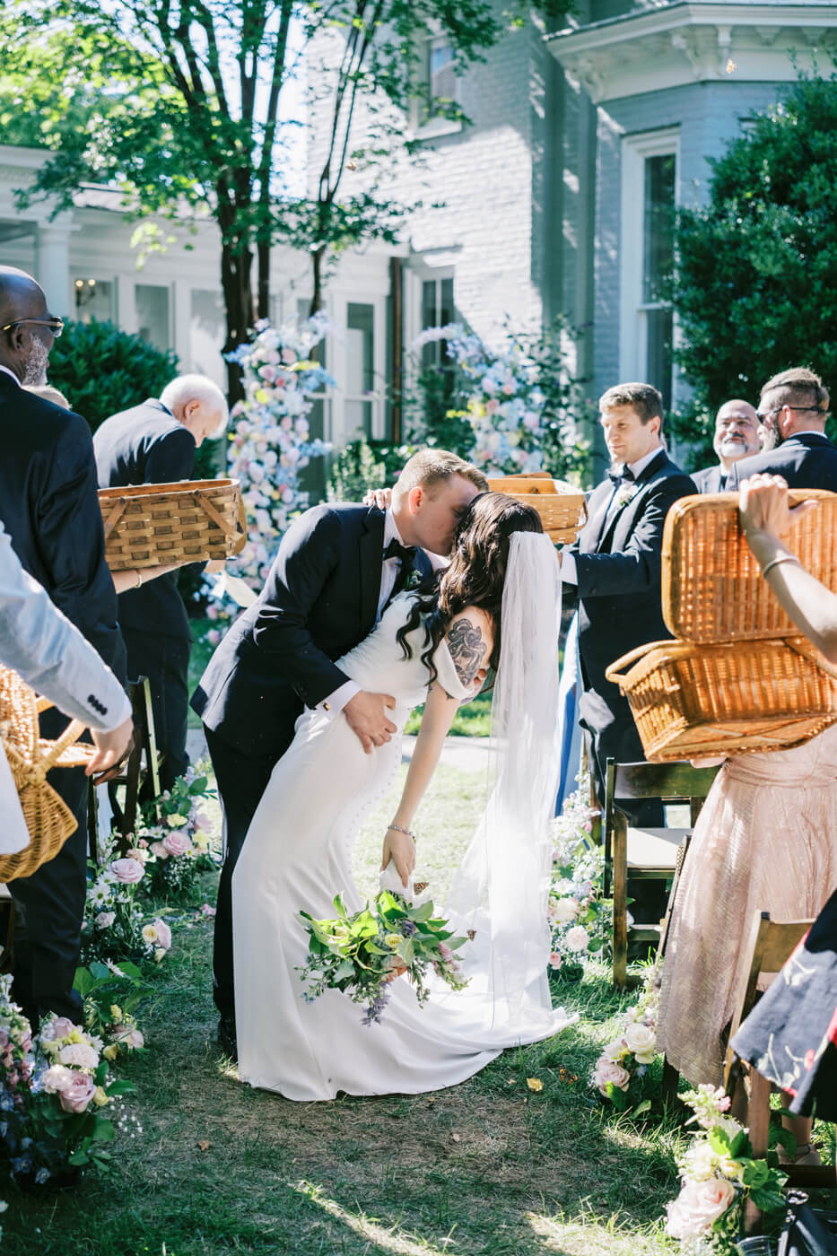 Romantic Newlywed Dip Kiss at Wedding Ceremony at the McAlister-Leftwich House – The groom passionately dips his bride for a kiss after their wedding ceremony, surrounded by family and friends holding woven baskets.