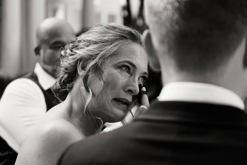 Emotional Mother-of-the-Bride Moment – A heartfelt black-and-white image captures the bride’s mother wiping away tears as she watches her daughter on her wedding day.