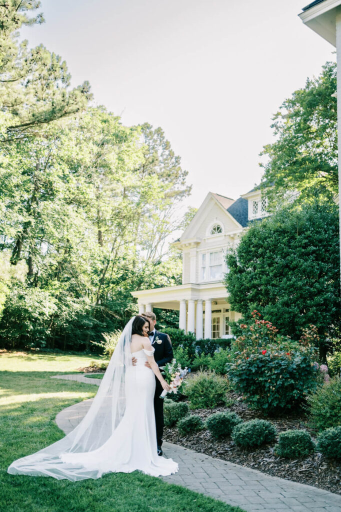 Romantic Bride and Groom Portrait at McAlister-Leftwich House – A groom embraces his bride in front of the stately McAlister-Leftwich House, capturing an intimate moment on their wedding day.