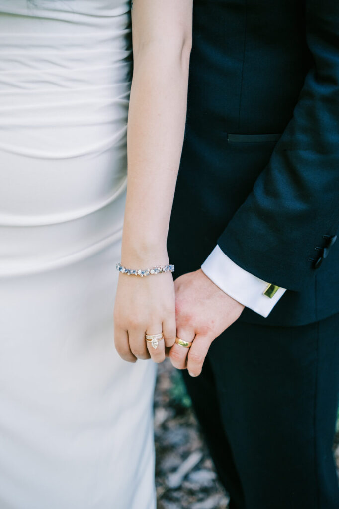 Close-up of Bride and Groom Holding Hands – A detailed shot of the bride and groom’s intertwined hands, highlighting their wedding rings and elegant attire.