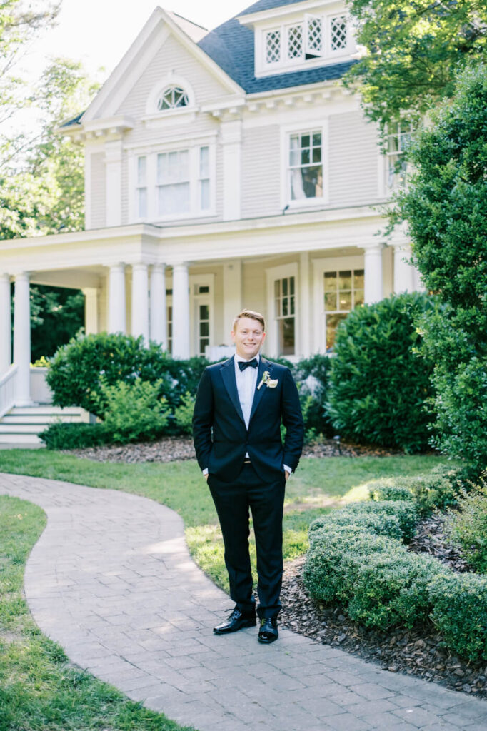 Groom Standing Confidently at McAlister-Leftwich House Wedding – A groom in a classic black tuxedo poses with a relaxed smile in front of the historic McAlister-Leftwich House.