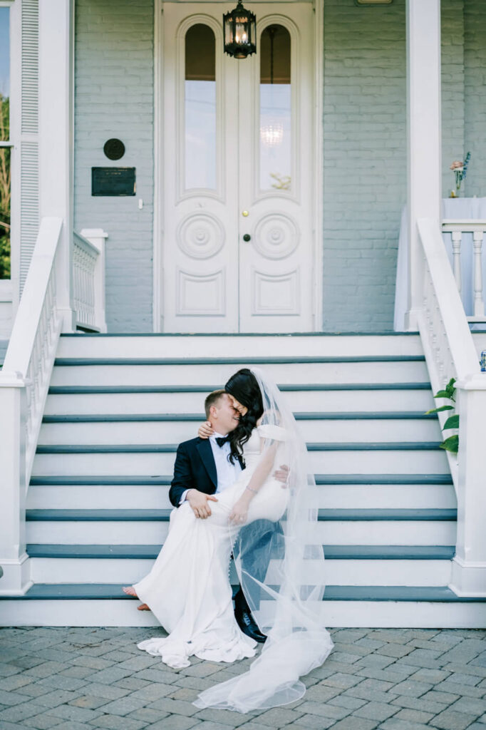 Bride and Groom Sitting on Grand Staircase – The bride and groom share a romantic embrace on the grand front steps of the McAlister-Leftwich House, showcasing timeless Southern elegance.