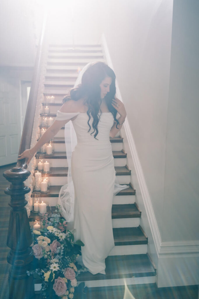 Bride Walking Down Candle-Lit Staircase – A bride gracefully descends a wooden staircase lined with glowing candles, bathed in dreamy soft light.