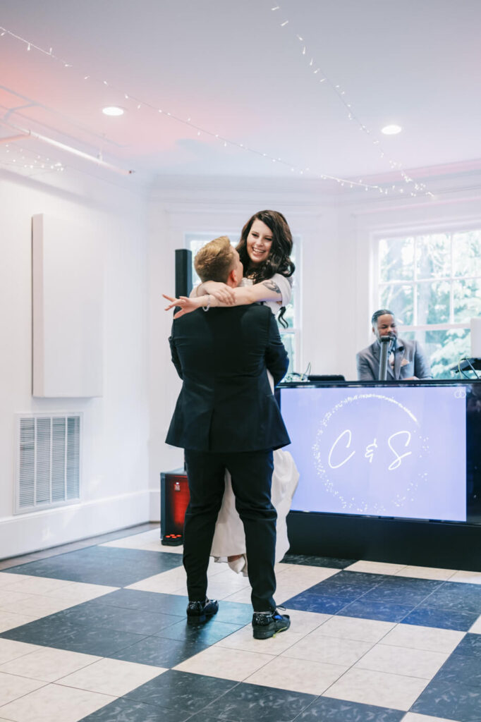 Bride and groom share a joyful first dance at McAlister-Leftwich House – The groom lifts his bride as she smiles, dancing in a beautifully lit reception space with their initials displayed behind them.