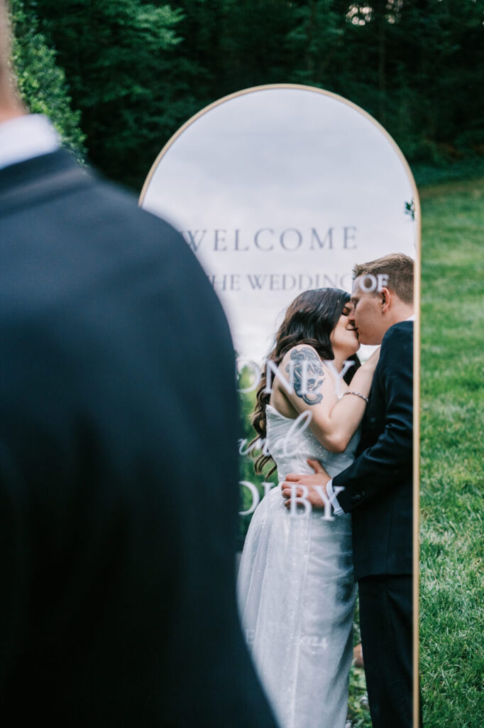 Bride and groom share a sweet kiss reflected in a welcome sign at their McAlister-Leftwich House wedding, adding a unique storytelling element to their love-filled day.