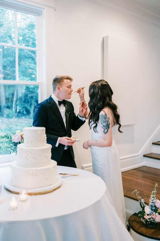 Bride and groom cut and share their elegant tiered wedding cake inside McAlister-Leftwich House, framed by warm candlelight and delicate floral arrangements.