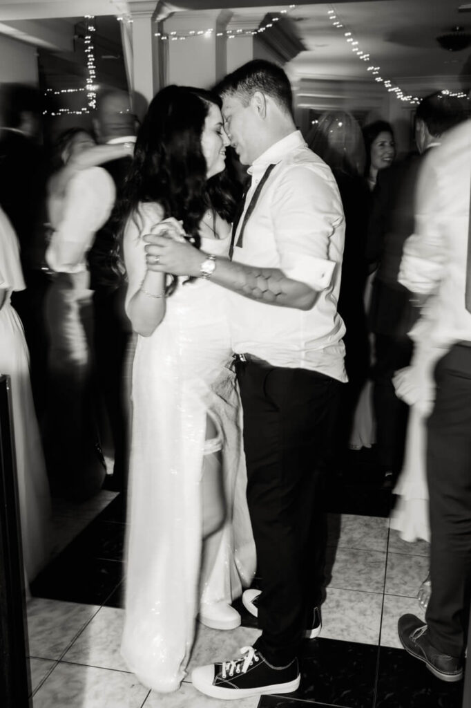 Bride and groom share a romantic dance under twinkling lights, their connection captured in a candid black-and-white moment at their Greensboro wedding.