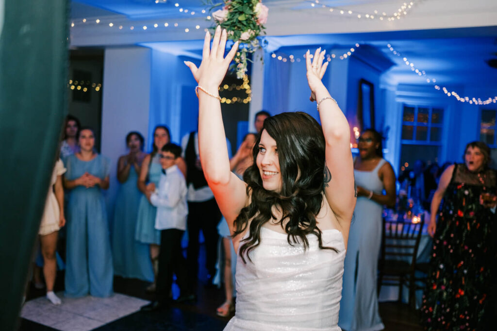 Bride tossing her bouquet during a lively wedding reception, as excited guests in blue bridesmaid dresses eagerly anticipate catching it.