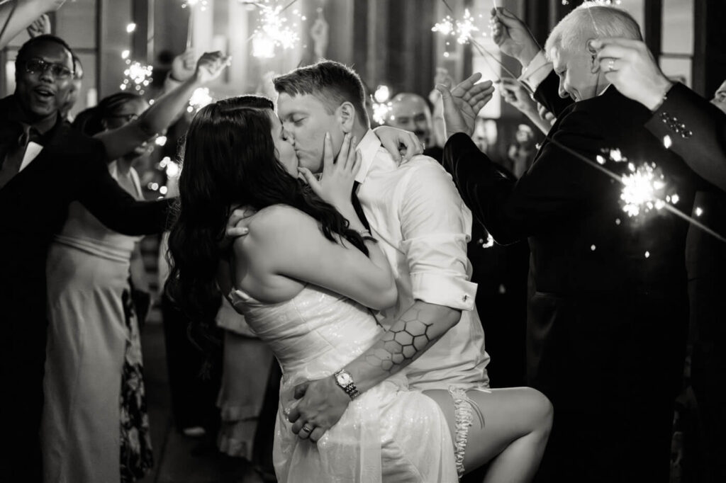 Newlyweds share a passionate kiss during their sparkler exit at McAlister-Leftwich House, surrounded by family and friends celebrating their love.