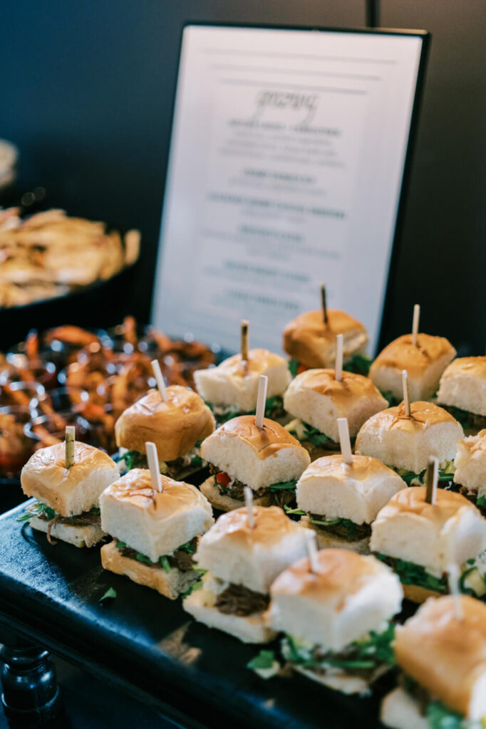 Close-up of gourmet sliders arranged on a black serving tray with a wedding reception menu in the background at McAlister-Leftwich House.