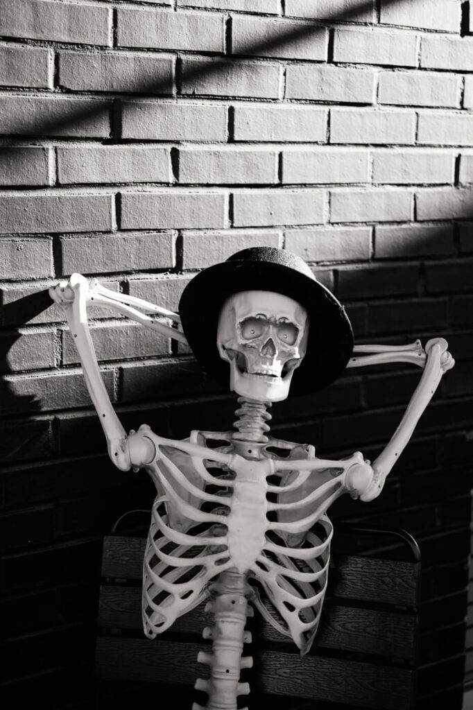 Black and white image of a decorative skeleton wearing a hat, posed against a brick wall at a stylish wedding rehearsal dinner.