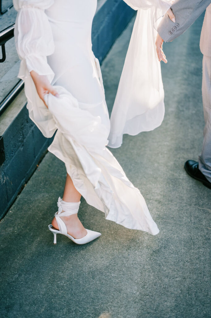 Bride's delicate white dress and strappy heels as she lifts her gown while walking at an intimate pre-wedding event in Greensboro, NC.