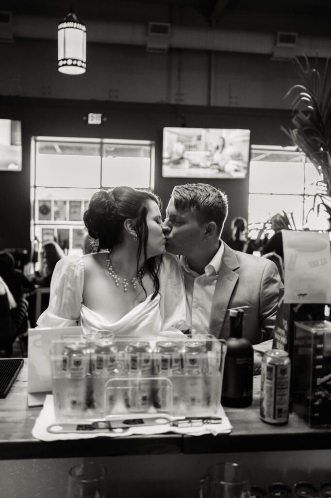 Bride and groom kissing at a dimly lit bar – A black-and-white photograph capturing the couple sharing a kiss at the bar, celebrating their love in a cozy Greensboro venue.