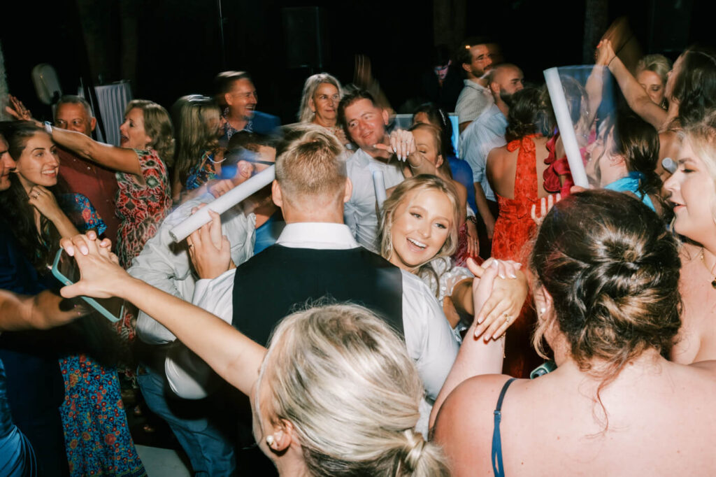 Epic dance floor celebration at an outdoor wedding reception – The bride and groom are at the center of an energetic wedding dance party, surrounded by friends and family under twinkling lights.