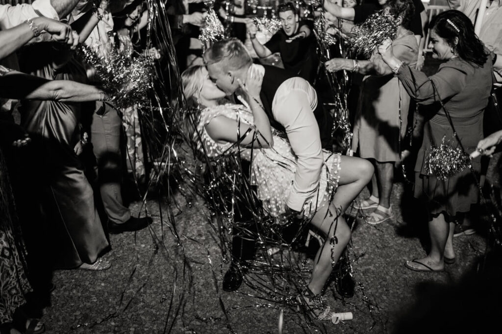 Bride and groom's dramatic wedding exit kiss – The groom dips his bride for a romantic kiss amid festive streamers as their guests cheer them on at The Historic Robertson House wedding.