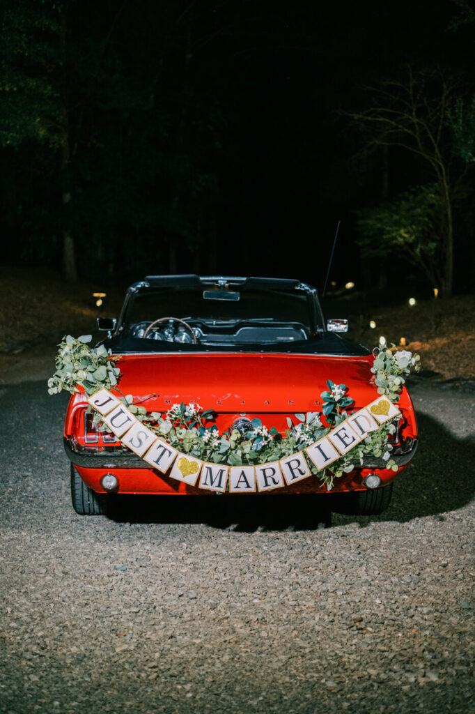 Classic red Mustang getaway car with 'Just Married' sign – A vintage Mustang convertible, decorated with lush greenery and a charming ‘Just Married’ sign, awaits the couple's grand exit.