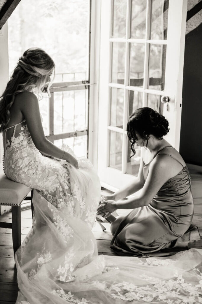 Bridesmaid kneeling to help the bride with her shoes in the elegant getting-ready room at Historic Robertson House.