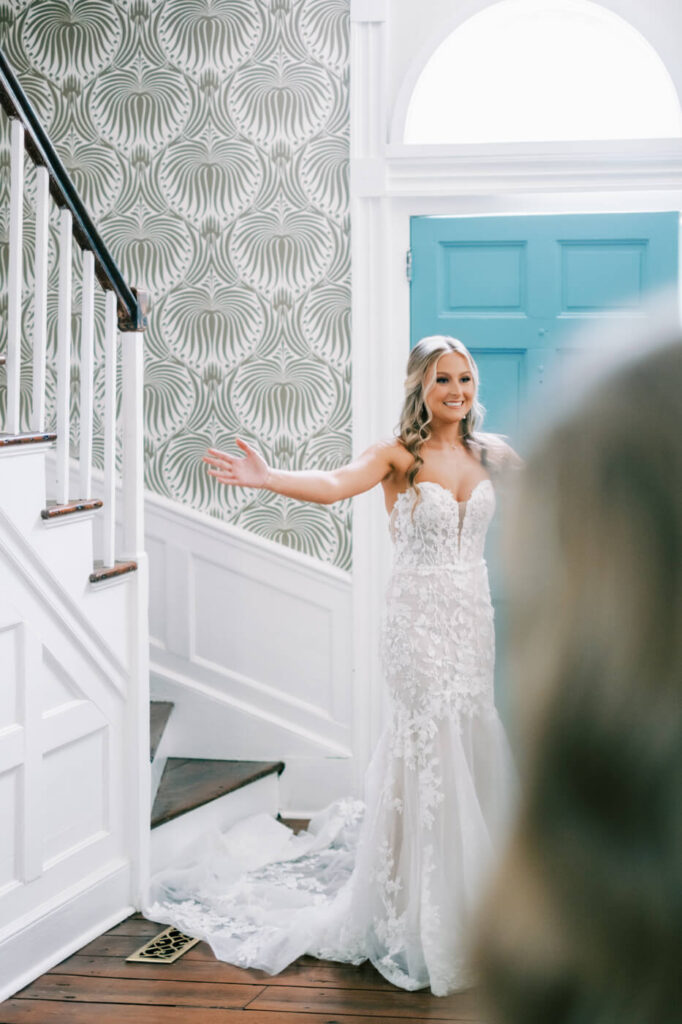 Bride joyfully revealing her wedding dress to her bridesmaids in the grand foyer of Historic Robertson House.