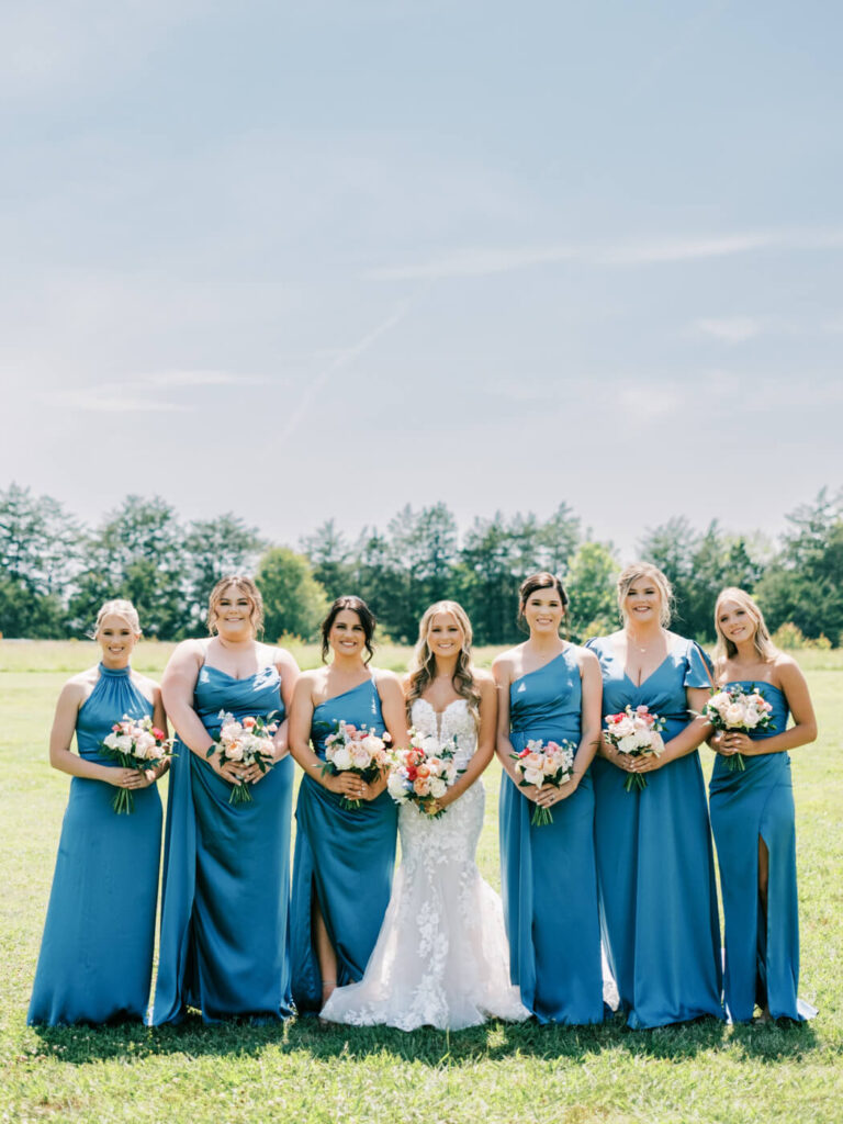 Bride with her bridesmaids in a sunlit field outside Historic Robertson House, holding pastel floral bouquets for a classic Southern wedding look.