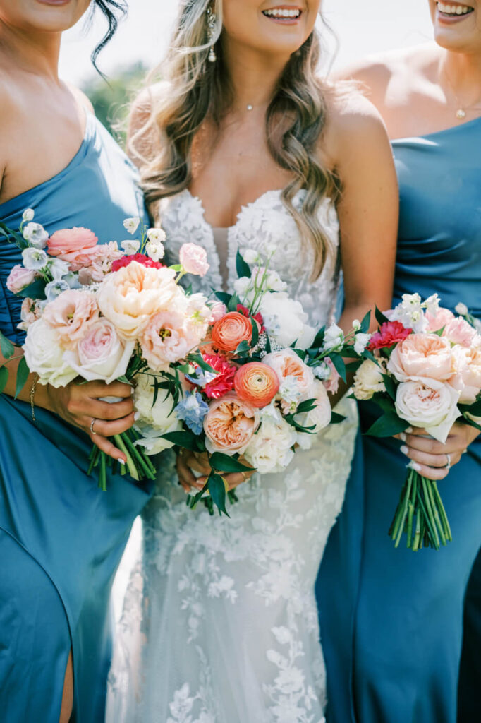 Close-up of the bride and bridesmaids holding lush floral bouquets, featuring blush roses and peach ranunculus at Historic Robertson House.