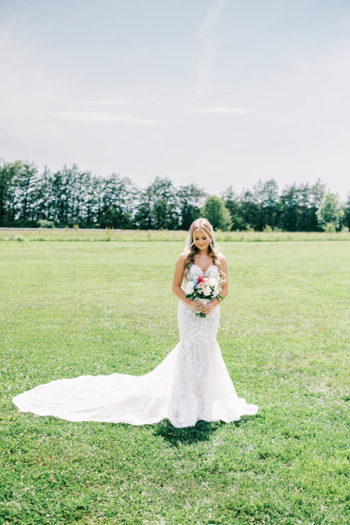 Bride standing alone in the meadow at The Historic Robertson House – A radiant bride in a lace wedding gown holds a floral bouquet, captured in a romantic and serene bridal portrait.