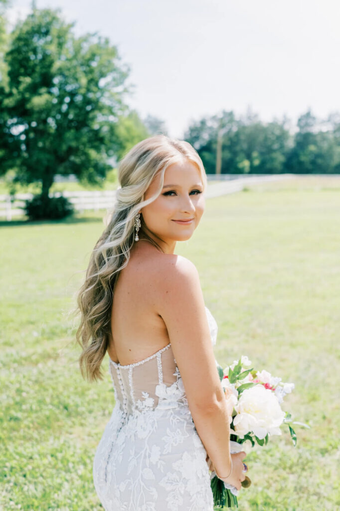 Close-up bridal portrait with soft curls and a delicate bouquet – A stunning bride glances back with soft, cascading curls and elegant bridal makeup, capturing a timeless wedding moment.