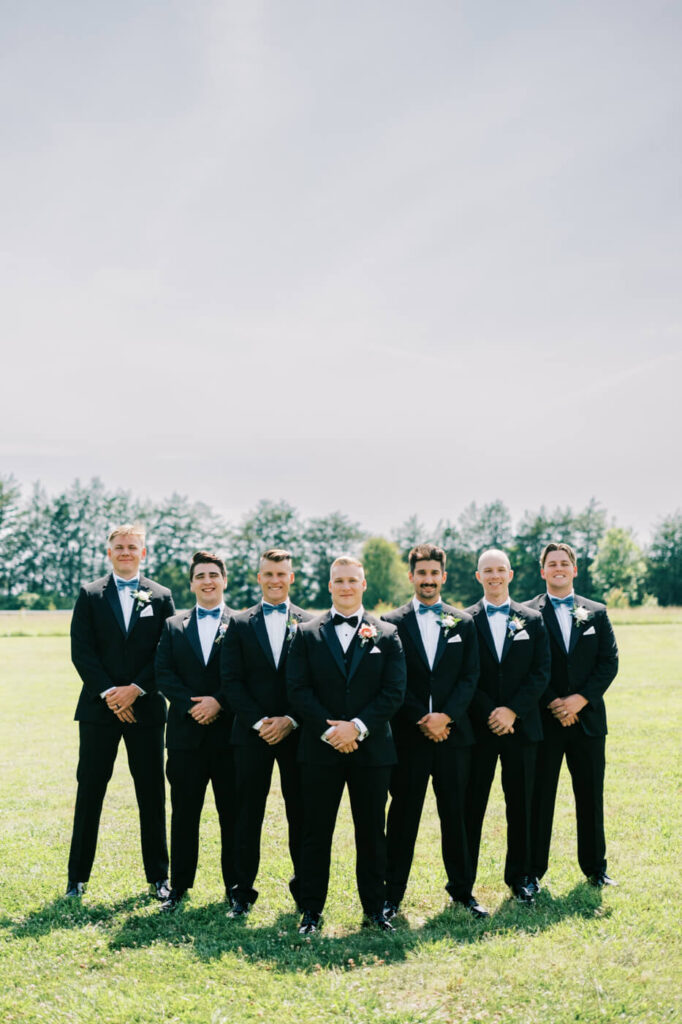 Groom and groomsmen in classic black tuxedos at The Historic Robertson House – The groom and his groomsmen pose in a lineup, exuding sophistication in traditional black tuxedos and blue bow ties.