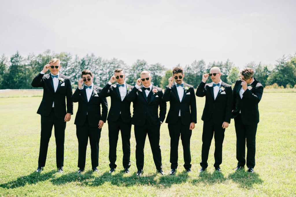 Groomsmen posing with sunglasses for a fun wedding photo – A stylish and playful moment as the groom and his groomsmen lift their sunglasses for a charismatic wedding day portrait.