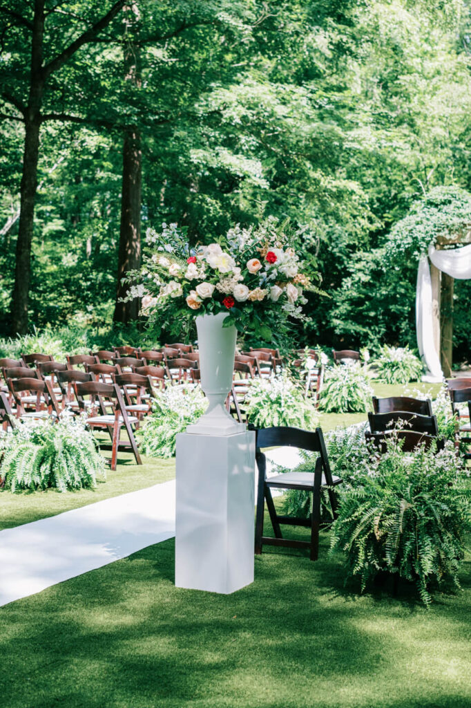 Scenic view of the wedding ceremony aisle surrounded by greenery – The picturesque wedding ceremony aisle at The Historic Robertson House, lined with white floral arrangements and ferns, creating an enchanting garden wedding ambiance.