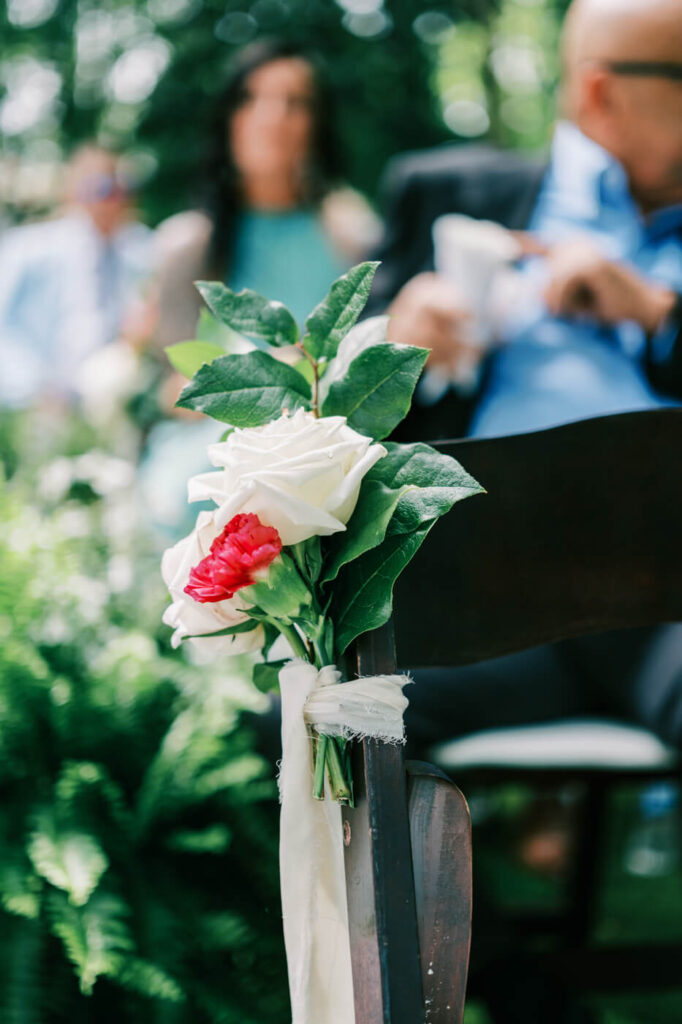 Floral chair decoration at an outdoor wedding ceremony – A close-up of a wooden ceremony chair adorned with a white and red rose bouquet, wrapped in flowing white fabric at The Historic Robertson House.