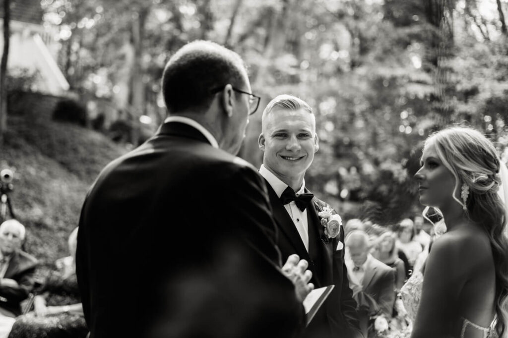 Black and white close-up of the groom’s emotional reaction during the wedding ceremony – A timeless black and white photograph captures the groom’s heartfelt smile as he looks at his bride during their vows.