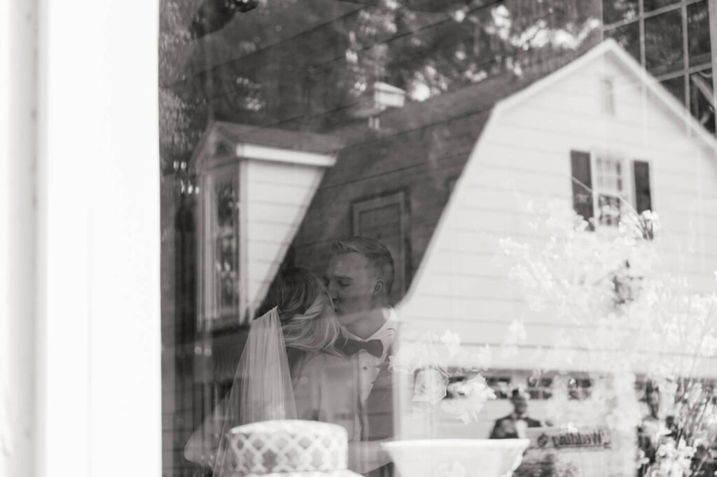 Black and white artistic shot of bride and groom sharing an intimate kiss through a vintage window reflection at the Historic Robertson House.