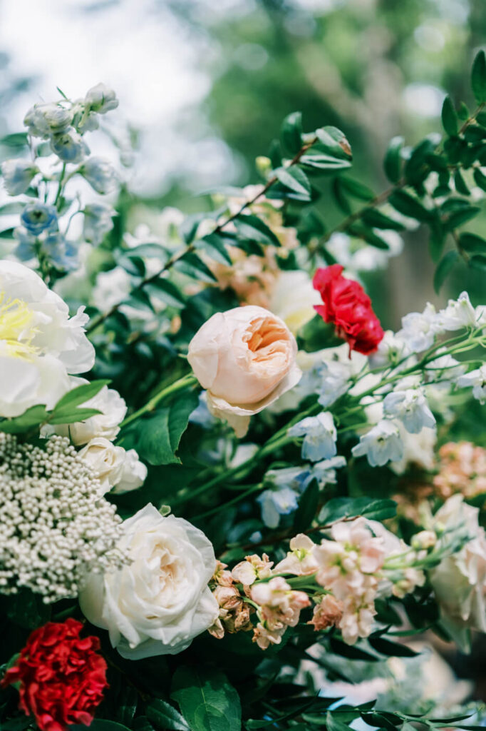 Close-up of a lush floral wedding arrangement featuring soft blush roses, blue delphiniums, and delicate greenery.