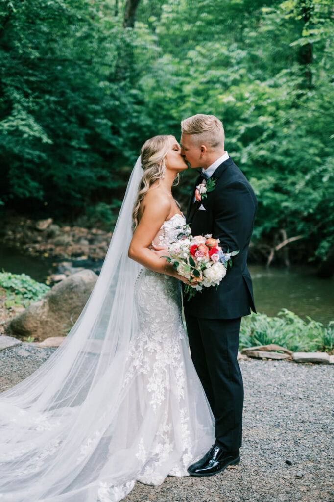 Romantic wedding portrait of the bride and groom sharing a kiss by the tranquil water’s edge at the Historic Robertson House.