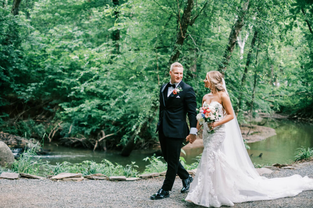 Newlyweds stroll hand in hand along a scenic garden path, the bride’s flowing lace gown trailing behind her, capturing a timeless wedding moment.