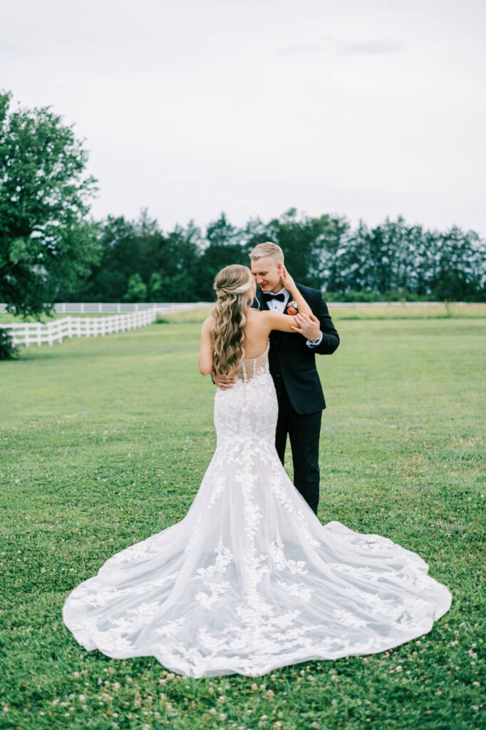 Bride and groom in a loving embrace on the lawn – A heartfelt wedding moment as the bride places her hands on the groom’s face, surrounded by the natural beauty of an open field.