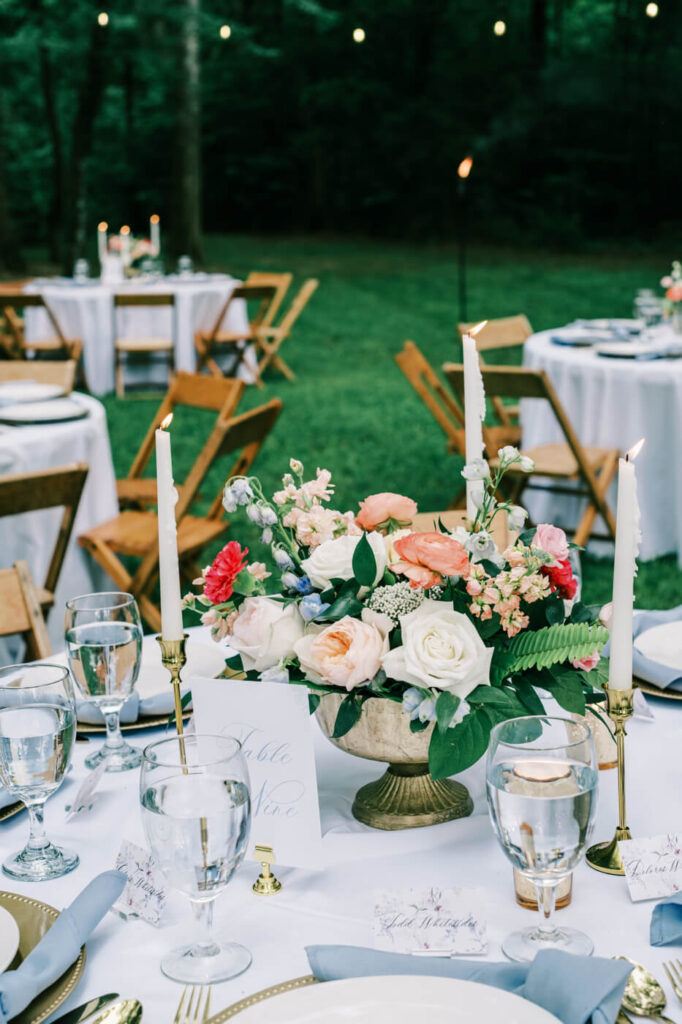 Lush garden-inspired wedding table decor – A stunning reception table featuring an elegant floral centerpiece with pastel roses, taper candles, gold-rimmed dinnerware, and handwritten place cards, creating a refined yet organic wedding aesthetic.