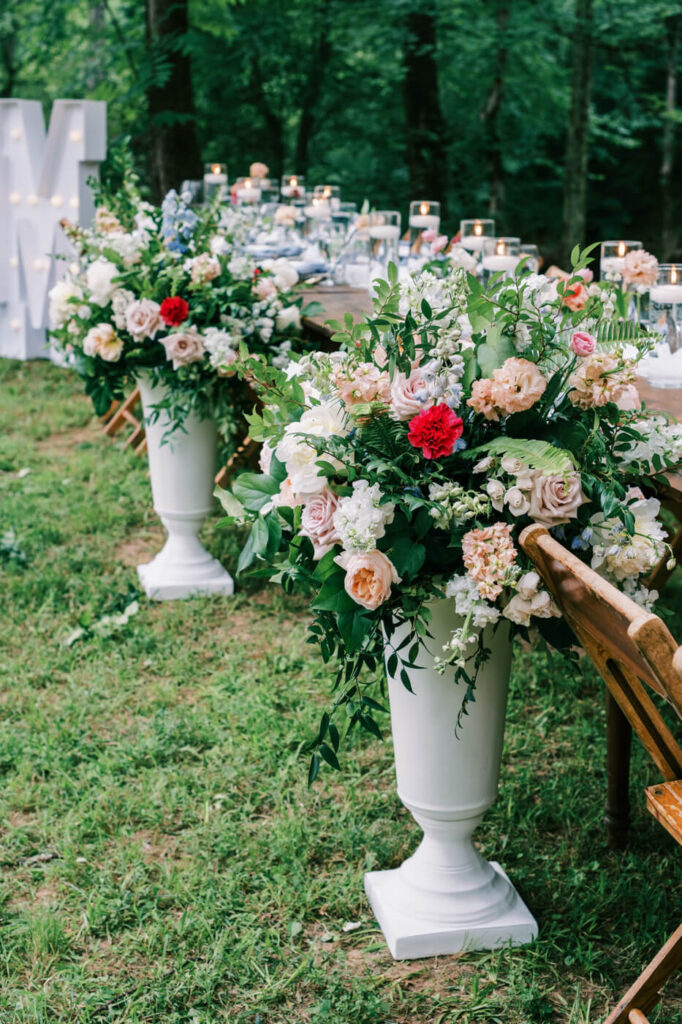 Floral aisle arrangements at The Historic Robertson House wedding – Tall white urns overflowing with blush, ivory, and red roses, accented with fresh greenery, line the wedding ceremony aisle in a picturesque outdoor setting.