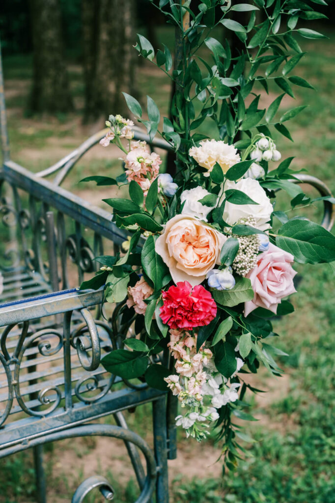 Romantic floral details on a vintage wedding cart – A close-up of lush floral arrangements featuring peach and ivory roses, soft blue accents, and rich greenery, decorating the ornate wedding cake cart at an outdoor reception.